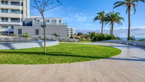 A modern hotel with a curved pathway, palm trees, and a view of the ocean.