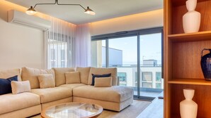 A modern living room with a beige sectional sofa, a glass coffee table, and a wooden bookshelf.