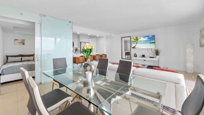 A modern living room with a glass dining table, white sofas, and a kitchen in the background. - Luxury Brickell Penthouse Ocean Views Rooftop Pool (Miami)