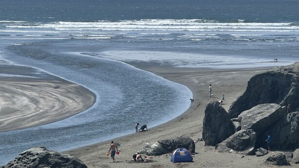 A beach with a tent, rocky outcrops, and people engaging in various activities.