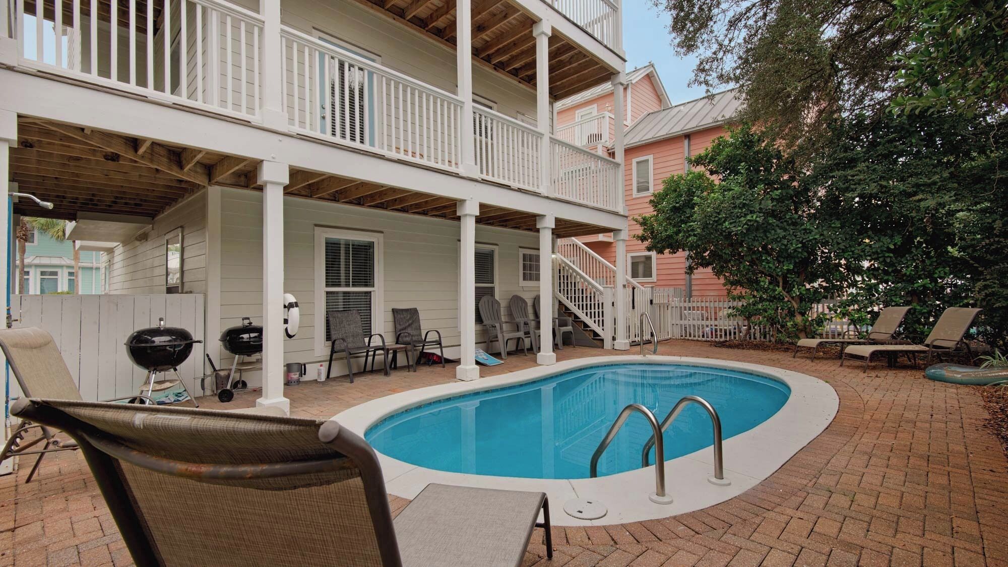 A pool area with a covered deck, lounge chairs, and a barbecue grill.