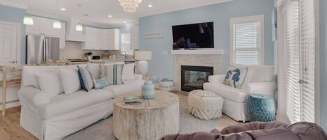 A modern living room with a fireplace, white sofas, a coffee table, and a TV mounted above the fireplace.
