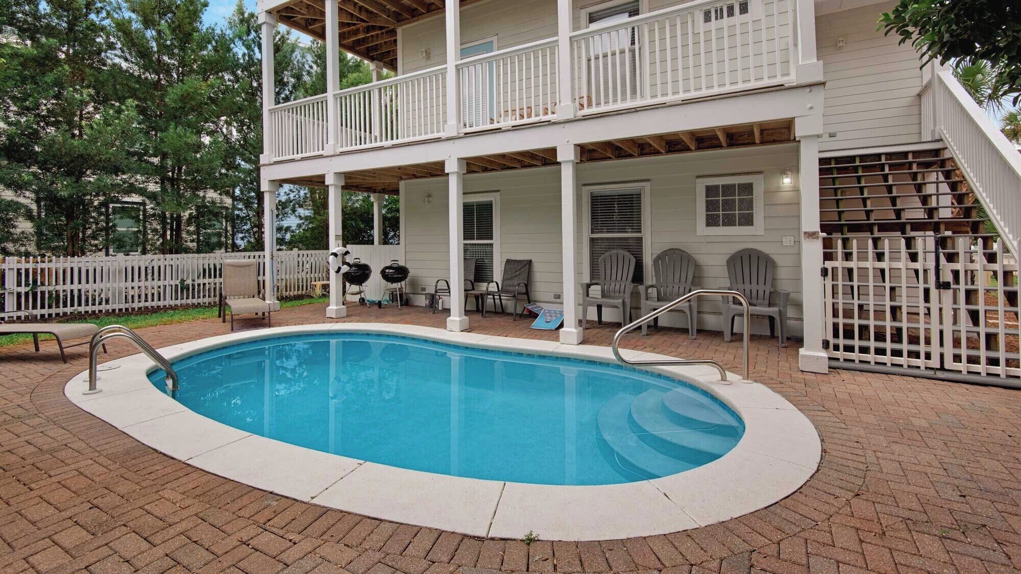 A two-story house with a covered patio area, a swimming pool, and outdoor seating.