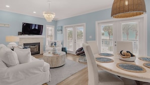 A living room with a fireplace, white furniture, a TV, and a dining area with woven placemats. - 4BR Home w/ Private Pool, Game Room, Beach Access! (Santa Rosa Beach)