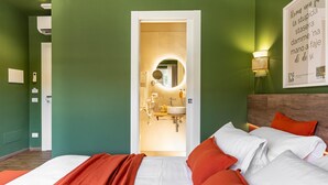 Habitación de hotel con cama, lámpara de noche, espejo y puerta que da a un baño.