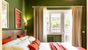 Una habitación de hotel con cama, almohadas, ventana con cortinas, pared con cita enmarcadas y radiador.