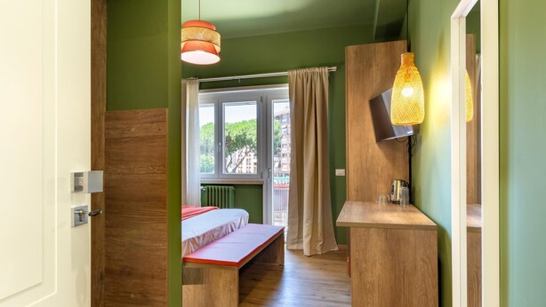 Una habitación con cama, banco, muebles de madera, una ventana con cortinas y una lámpara colgante.