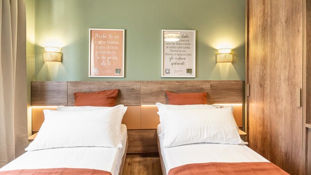 A hotel room with two beds, wooden headboard, wall-mounted lights, and two framed quotes on the wall. - Elegant Double Room in the Heart of the Peaceful Colli Albani Area (ROMA)