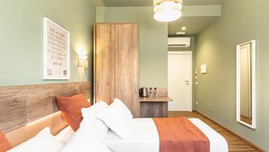 A hotel room with a bed, a wooden wardrobe, a small table with a kettle, and a wall-mounted mirror. - Elegant Double Room in the Heart of the Peaceful Colli Albani Area (ROMA)