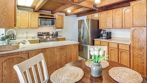 A kitchen with wooden cabinets, stainless steel appliances, and a dining area with woven placemats and a vase of flowers. - Grill & Games: Family-Friendly Flagstaff Getaway! (Flagstaff)