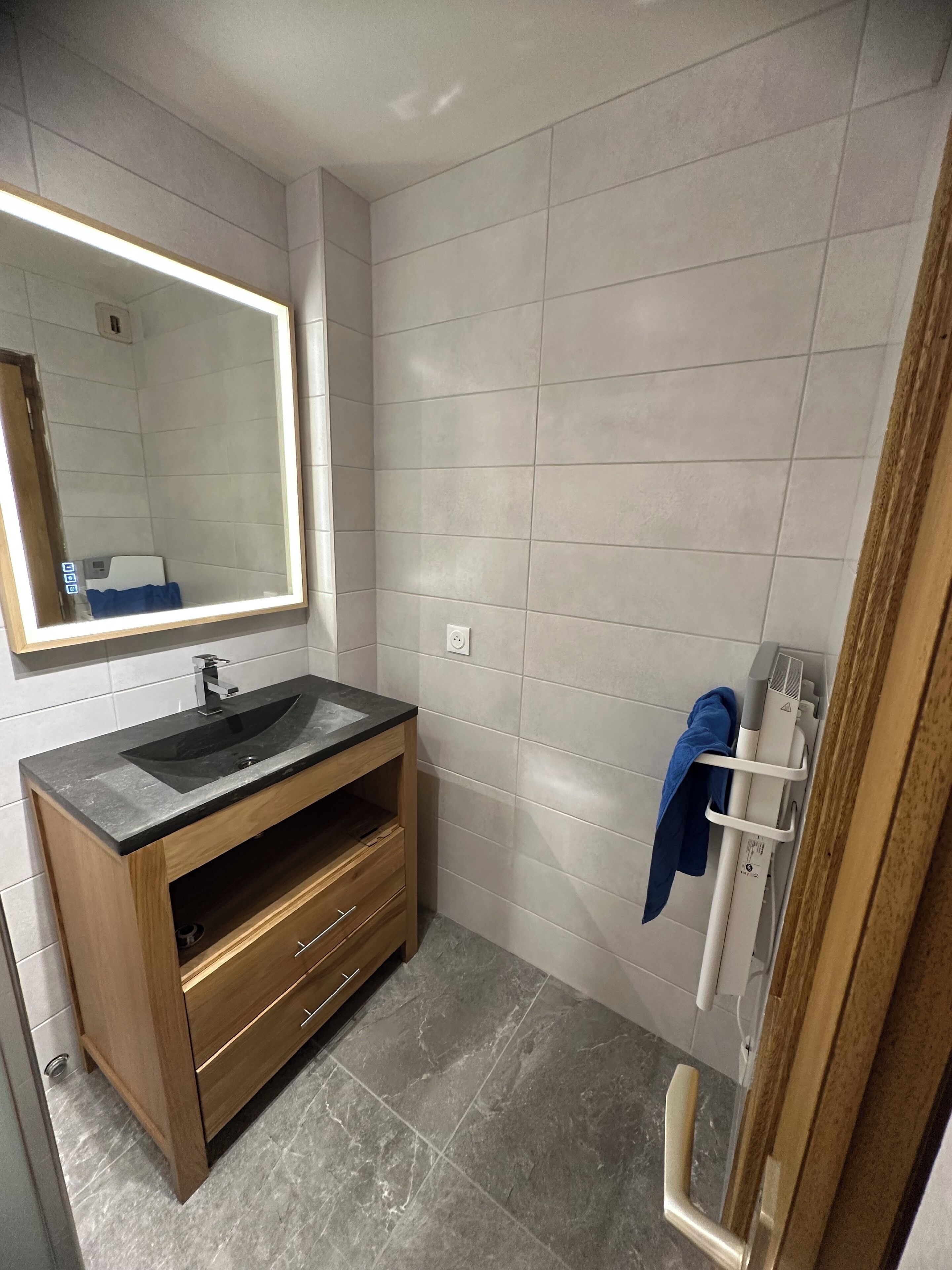 A modern bathroom with a large mirror, a wooden vanity with a sink, and a towel rack.