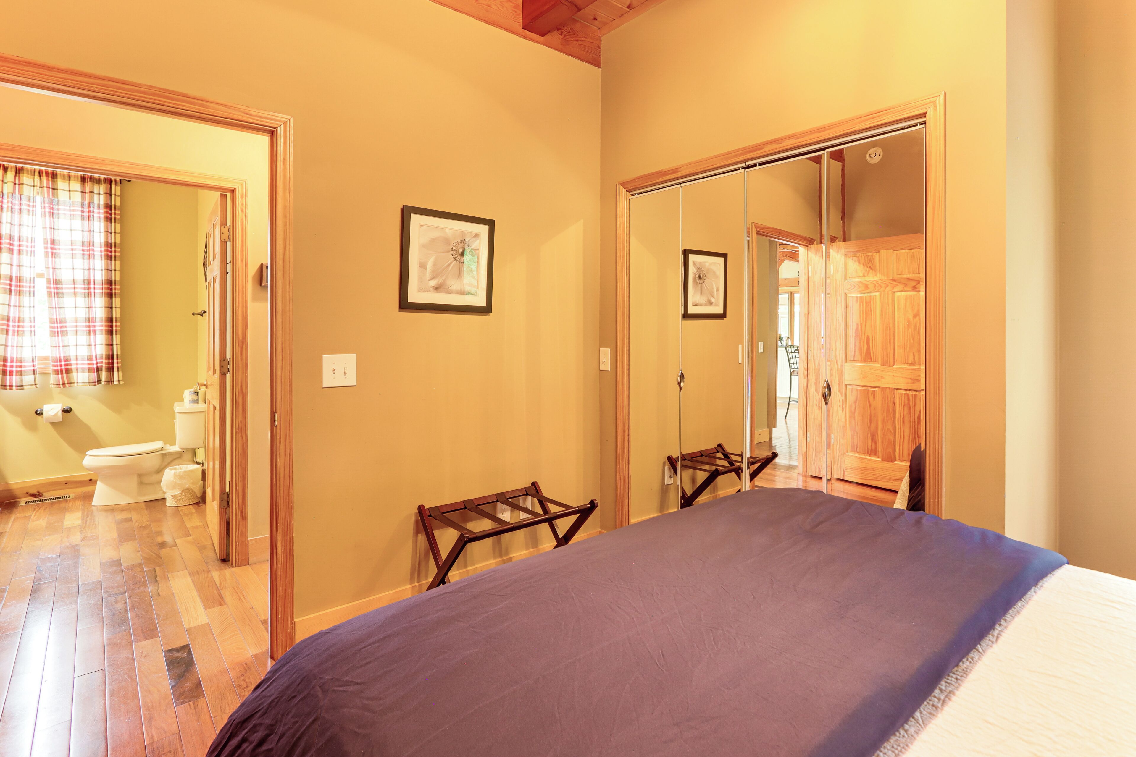 Een slaapkamer met een bed, een houten garderobe en een badkamer door een open deur zichtbaar.