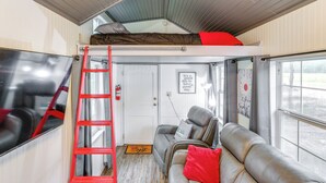 Ett kompakt bostadsutrymme med en våningssäng, en soffa, en tv och en stege.