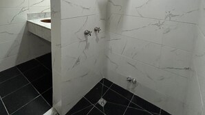 A bathroom with white marble walls, a black tiled floor, a shower with a handheld showerhead, and two faucets. - Suites Lima (Buenos Aires)