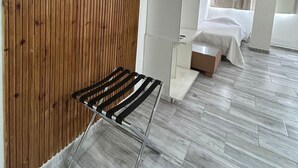A modern hotel room with a wooden panel wall, a flat-screen TV mounted above a metal rack, a bed with a white bedspread, and a large window with curtains. - Suites Lima (Buenos Aires)