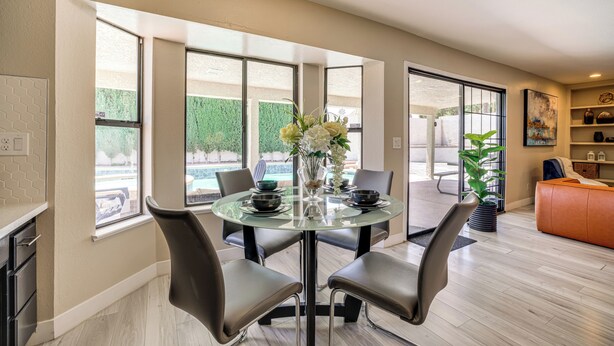 Un área de comedor moderna con una mesa de vidrio, cuatro sillas y un jarrón de flores.