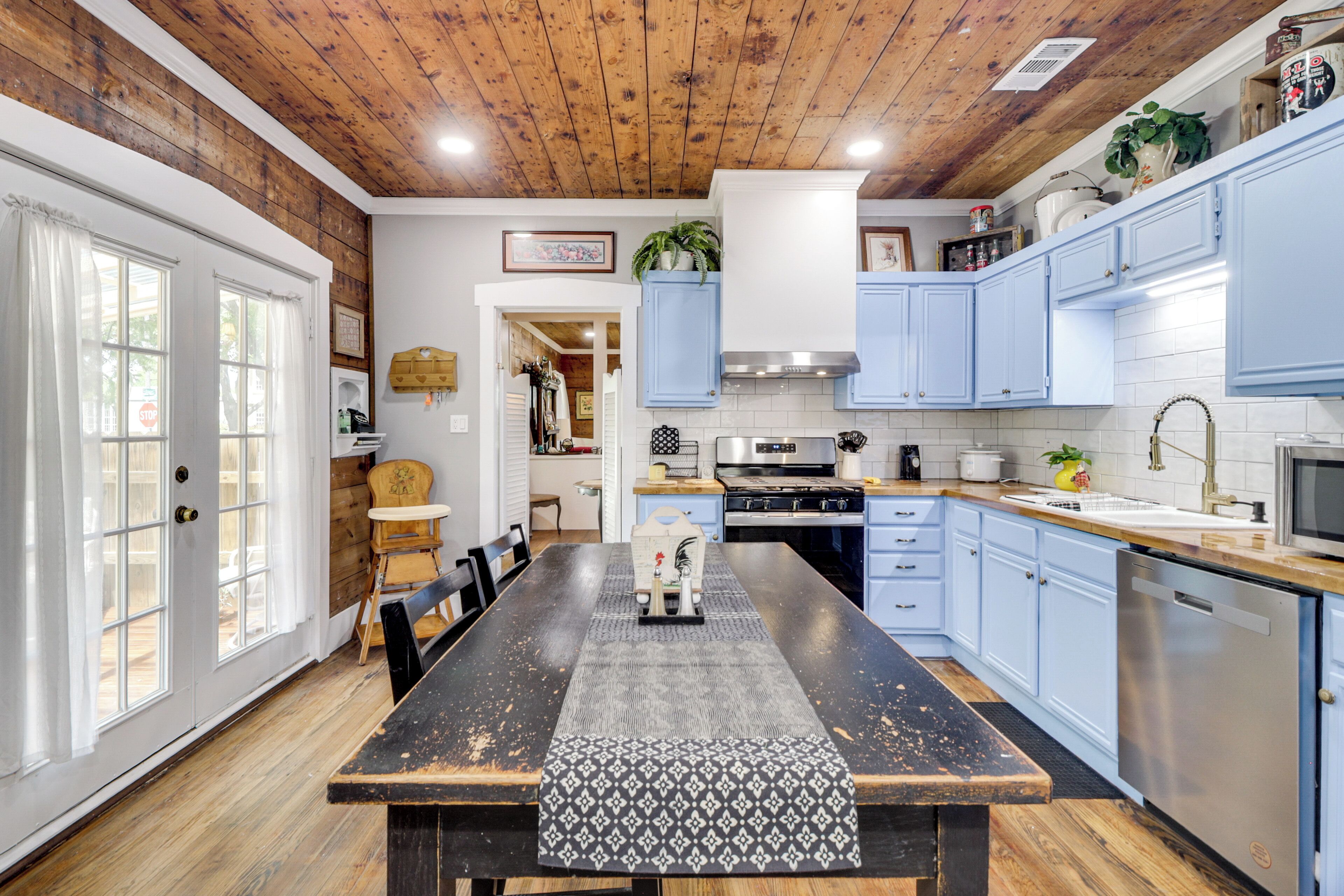 A kitchen with a wooden ceiling, light blue cabinets, a central island, and a dining area with a table and chairs.