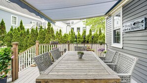 A wooden deck with a table and wicker chairs, surrounded by potted plants and a white picket fence. - North Shore Townhome: 1 Mi to Singing Beach! (Manchester-by-the-Sea)