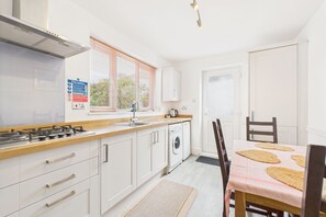 Una cocina moderna con armarios blancos, estufa a gas, lavamanos y ventana con persianas.