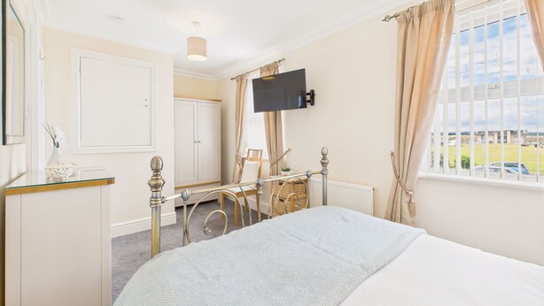 A bedroom with a bed, a TV mounted on the wall, a window with curtains, and a view of the outside.