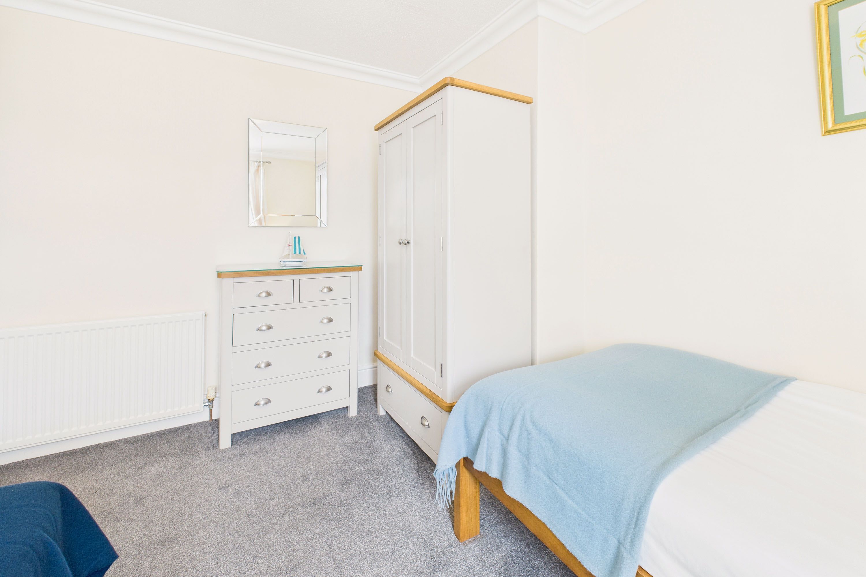 Un dormitorio con cama, armario, cómoda, espejo y radiador.