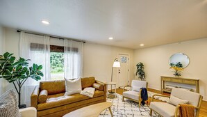 A living room with a brown sofa, a white armchair, a small table, and a floor lamp. - 7 Mi to Mt Rainier NP: Home w/ Private Hot Tub! (Ashford)
