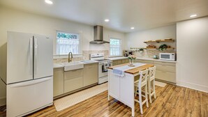 A modern kitchen with white appliances, wooden flooring, and a central island with bar stools. - 7 Mi to Mt Rainier NP: Home w/ Private Hot Tub! (Ashford)