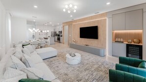 A modern living room with a large TV, a sofa, and a dining area in the background. - Amazing 7 bd Summerkitchen Gameroom (Clermont)