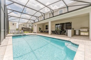 Una piscina con una zona patio coperta, posti a sedere all'aperto e un barbecue.