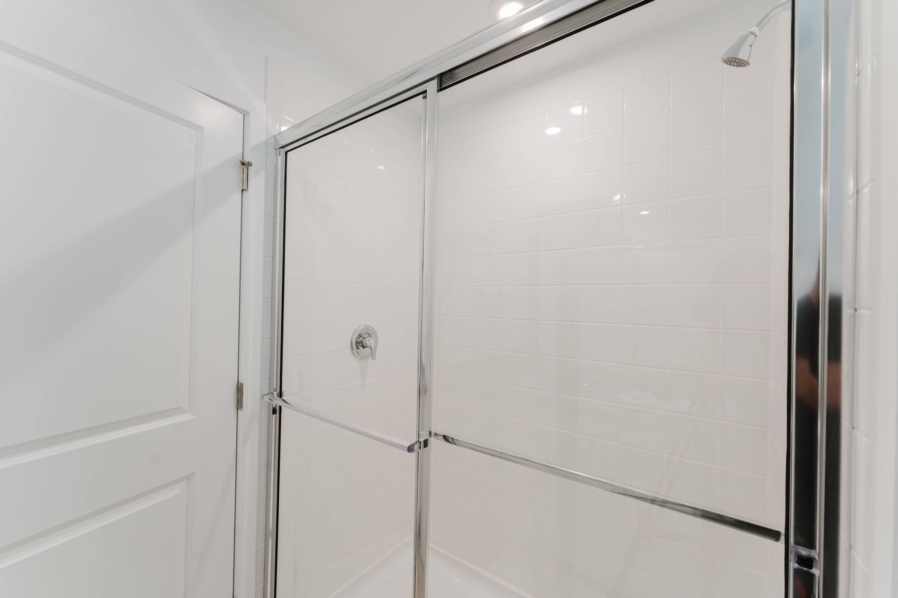 A modern bathroom with a glass shower enclosure, white tiled walls, and a visible showerhead.