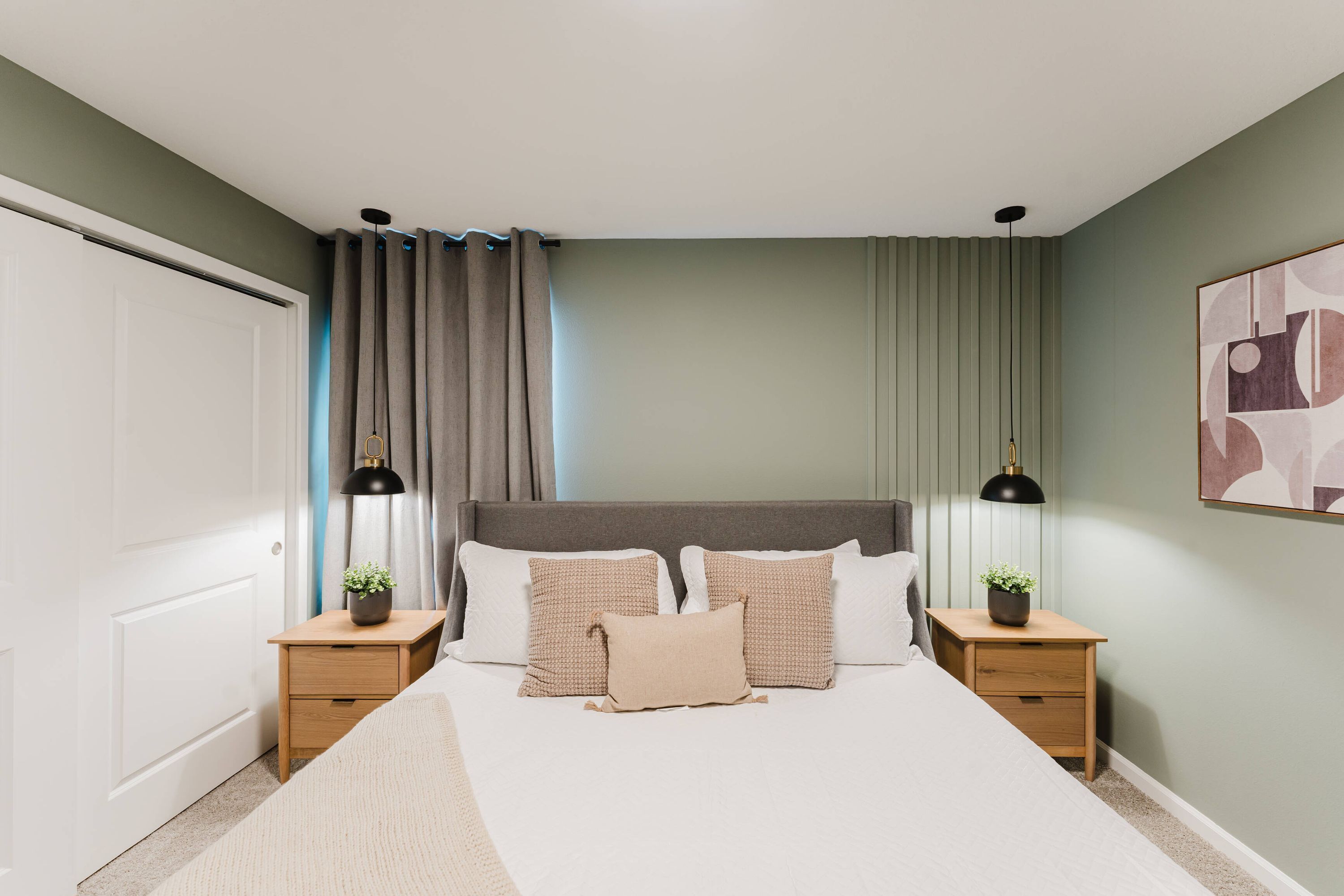 A bedroom with a bed, two bedside tables, a nightstand, a lamp, and a wall-mounted artwork.