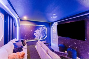 Un'elegante sala home theater con un grande televisore piatto, sedute confortevoli e un murale a tema spaziale.