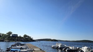 Un puerto deportivo con barcos amarrados, un muelle de madera y una isla boscosa al fondo.
