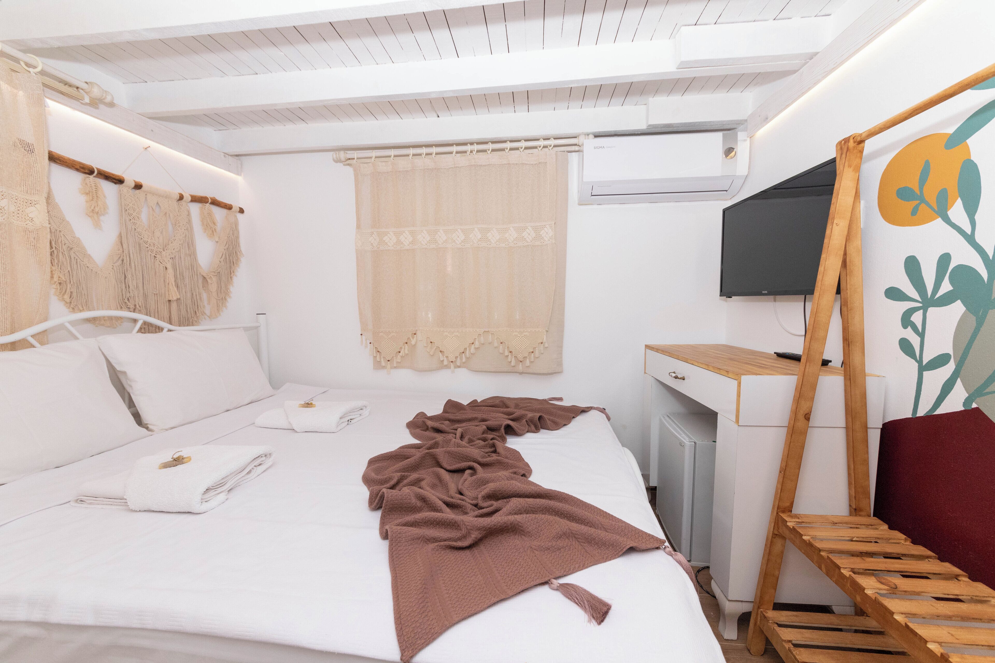 A bedroom with a bed, a desk, a TV, and a window with curtains.
