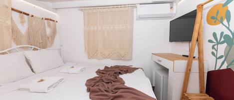 A bedroom with a bed, a desk, a TV, and a window with curtains.
