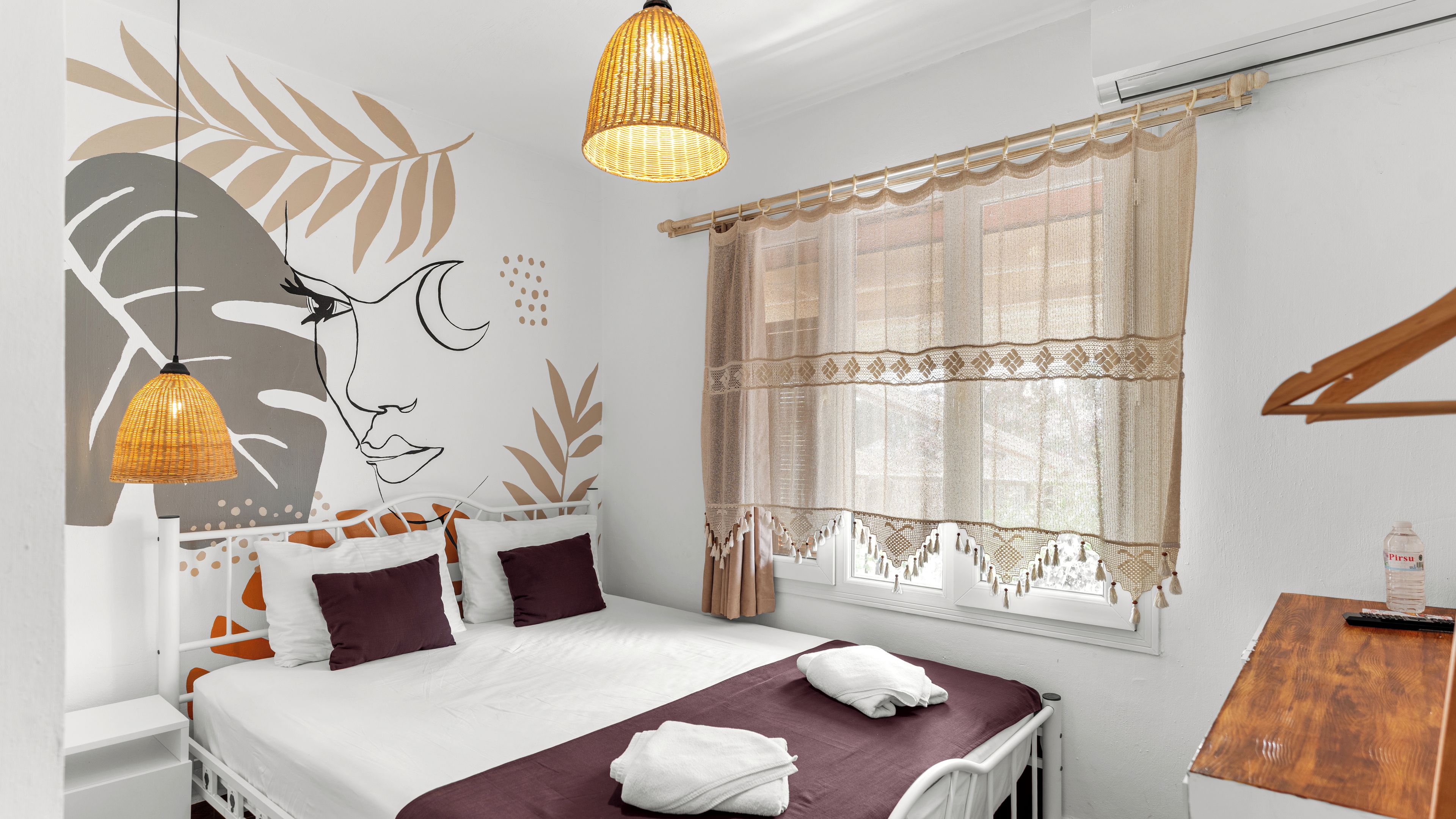 Un dormitorio con cama, dos mesitas de noche, lámpara colgante, ventana con cortinas y un papel tapiz con diseño de hojas.