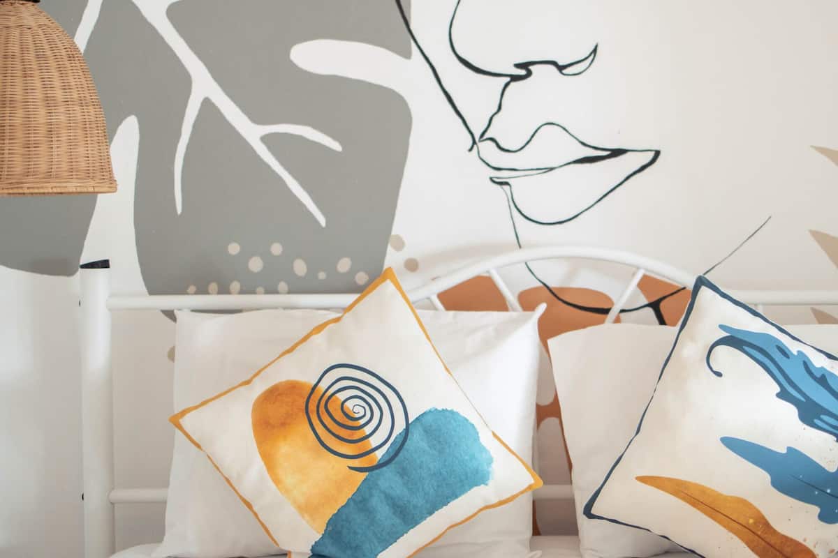 Un letto con biancheria da letto bianca e tre cuscini decorativi con motivi astratti.