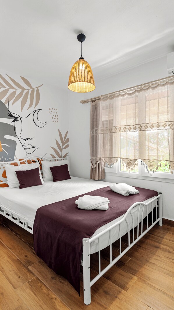 A bedroom with a bed, a hanging light fixture, a window with curtains, and a wall with a leaf pattern. - Casa Fiore (Seferihisar)
