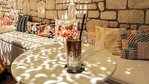 A glass of iced coffee on a round table with a stone wall in the background.