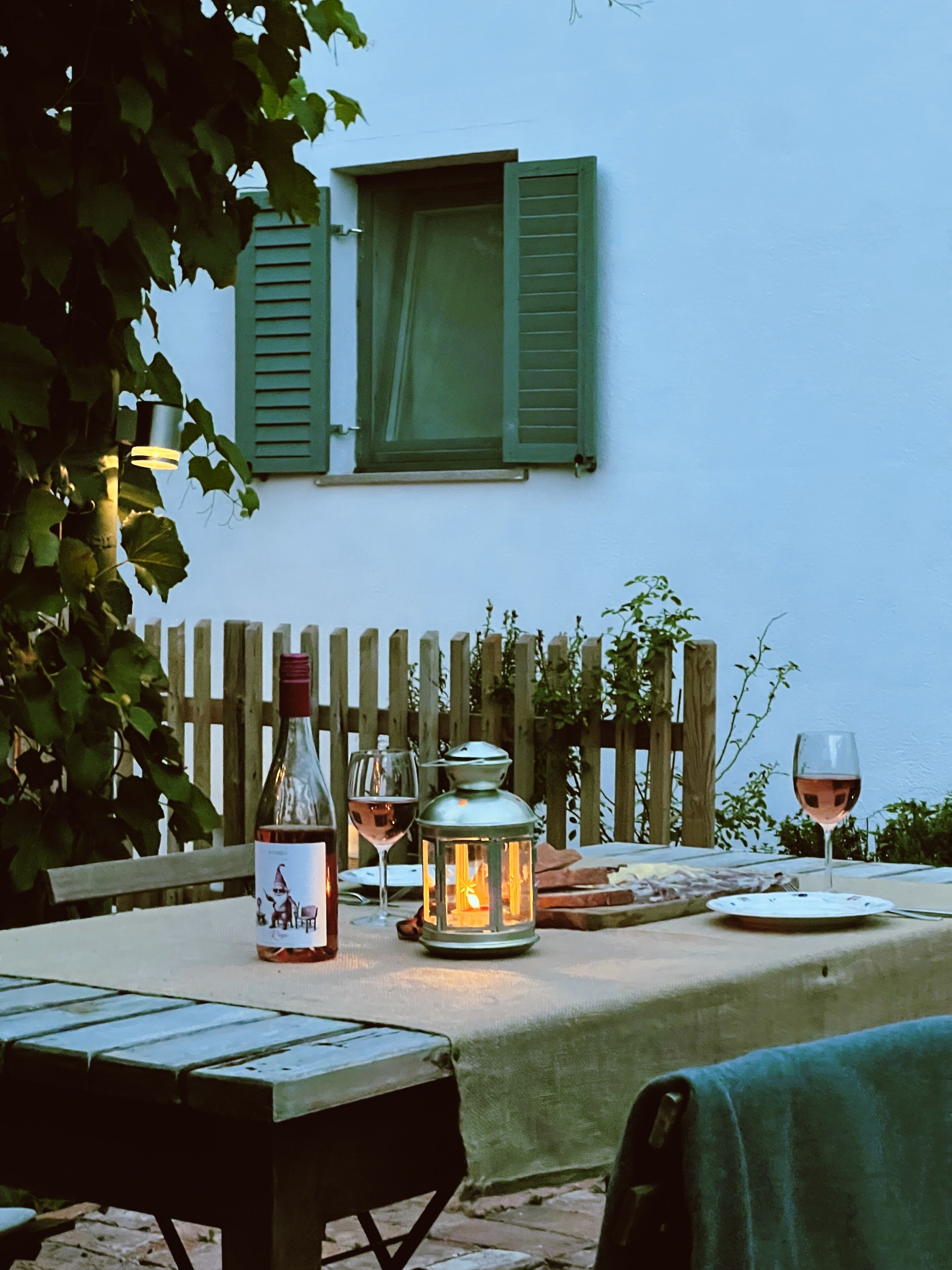 An outdoor dining table with a bottle, wine glasses, and a lantern.