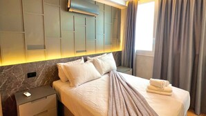 Una habitación de hotel moderna con una cama grande, una mesita de noche, aire acondicionado integrado y una ventana con cortinas.