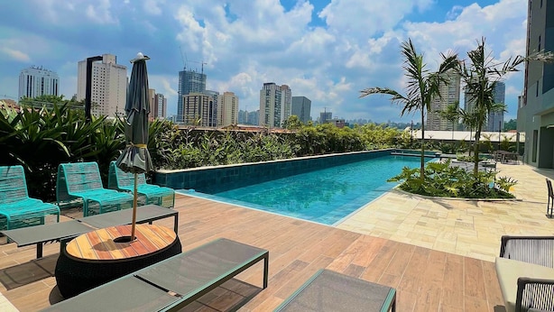 Un área de piscina en la azotea con sillas de descanso y una mesa, rodeada por un paisaje urbano.