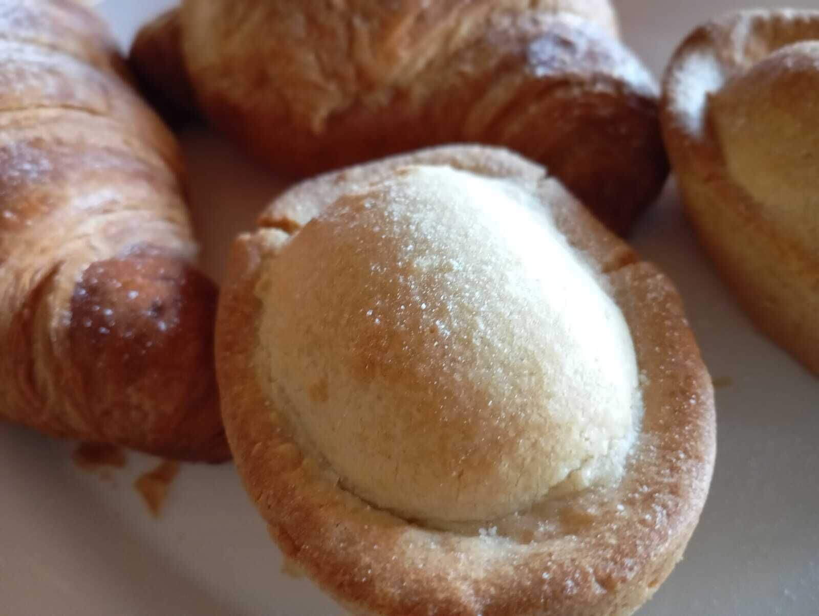 En tallrik med flera bakverk, bland annat en croissant och en liten paj med en klick grädde.