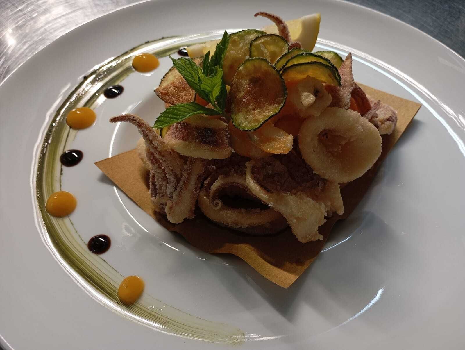 A plate with a dish of food, including what appears to be fried items and garnishes, on a white plate with a decorative edge.