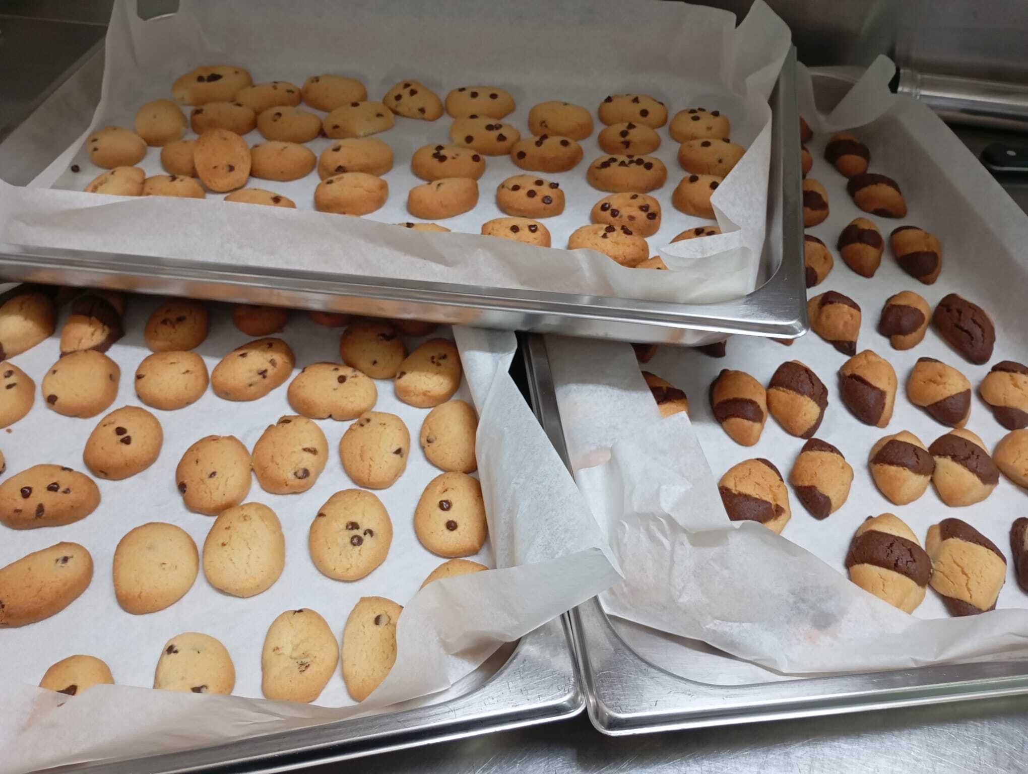 Bakplaten met taaltjes, waarschijnlijk koekjes, bekleed met bakpapier.