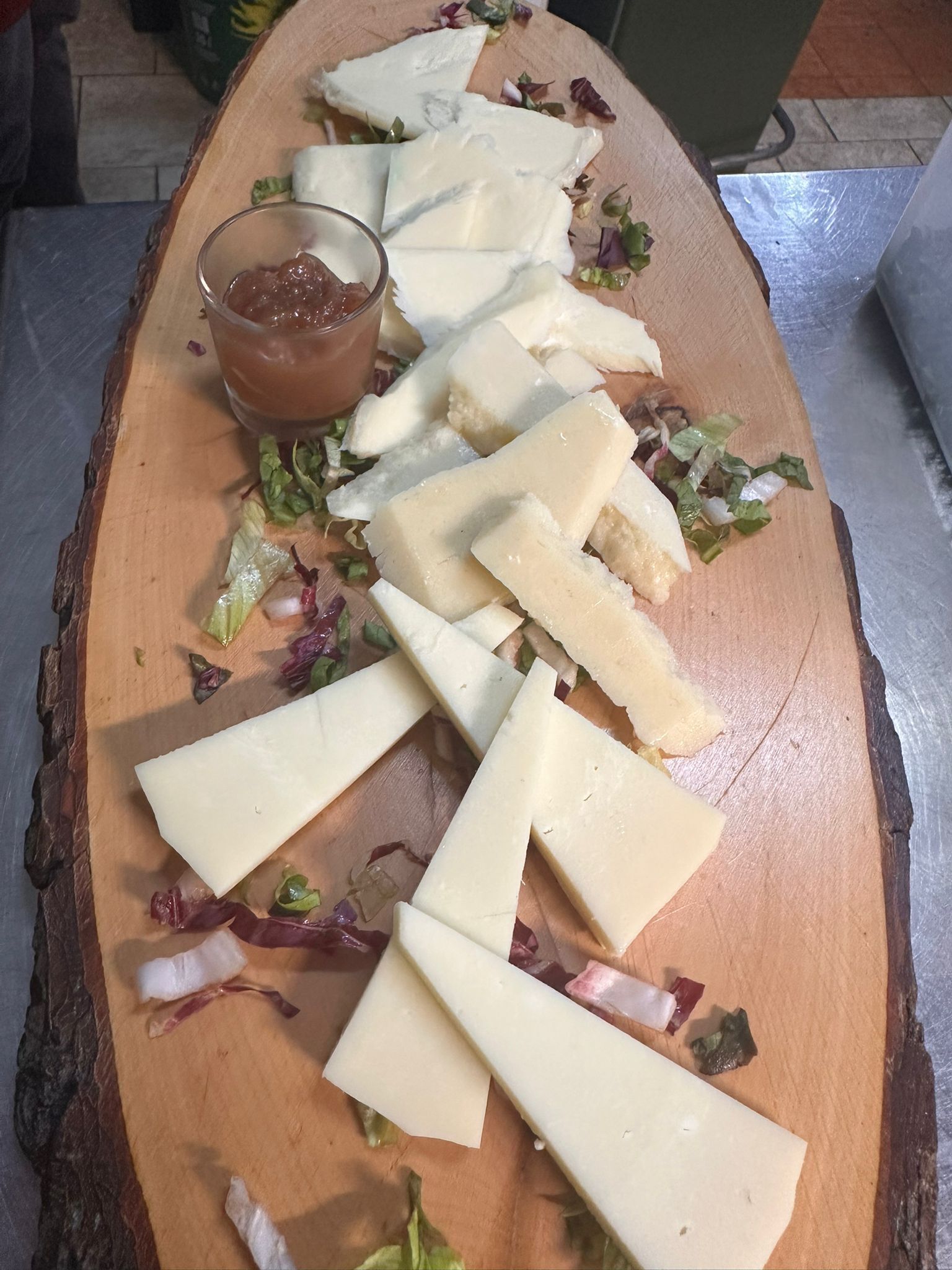 A wooden board with cheese slices, some lettuce, and a small bowl of sauce.