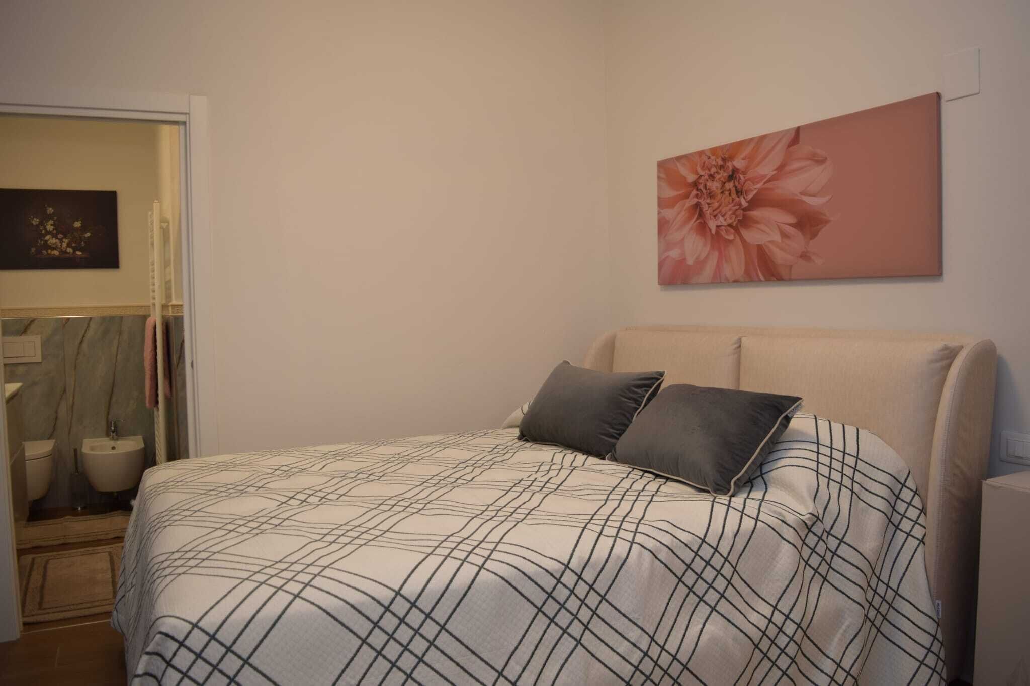 A bedroom with a bed, a large floral artwork on the wall, and a bathroom visible through an open door.
