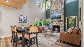 A spacious living area with a stone fireplace, a dining table with chairs, and a comfortable seating area with a sofa and a coffee table.