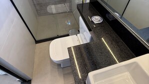 Un bany modern amb una cabina de dutxa de vidre, un vàter blanc i un taulell de granat negre.