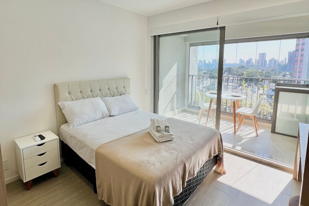 Ein modernes Schlafzimmer mit einem großen Bett, einem Nachttisch mit Telefon und Blick auf eine Stadtlandschaft vom Balkon aus.